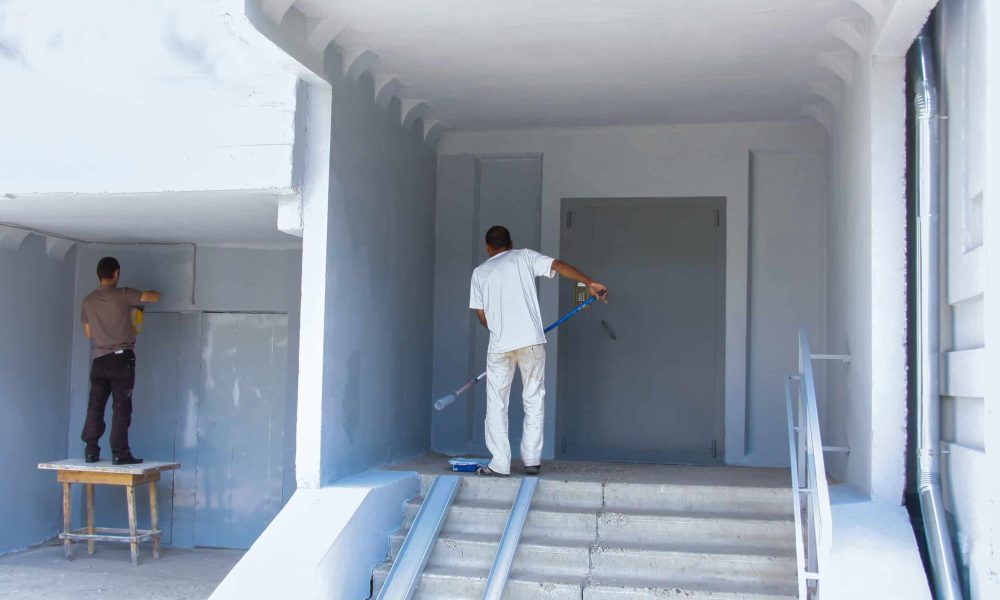 Workers paint the facade of a residential, apartment building. Painting work on the street. Back view. No faces.