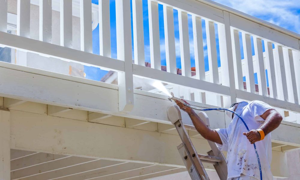 House Painter Wearing Facial Protection Spray Painting A Deck of A Home.